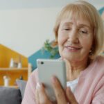自宅でスマートフォンを使用するシニア女性。文字の見やすさと通知設定を確認するイメージ