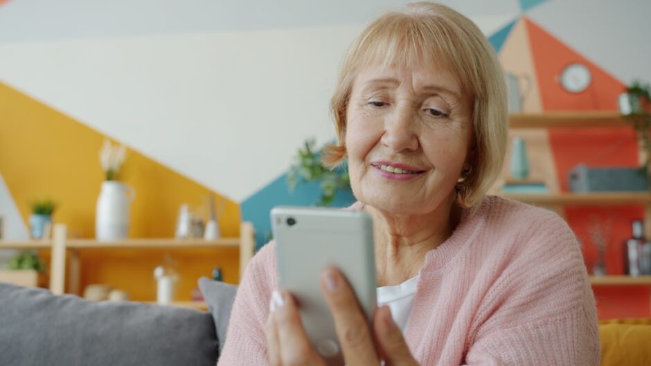 自宅でスマートフォンを使用するシニア女性。文字の見やすさと通知設定を確認するイメージ