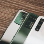 木のテーブルに並んだ2台のスマートフォン。古いスマホから新しいスマホへのデータ移行のイメージ